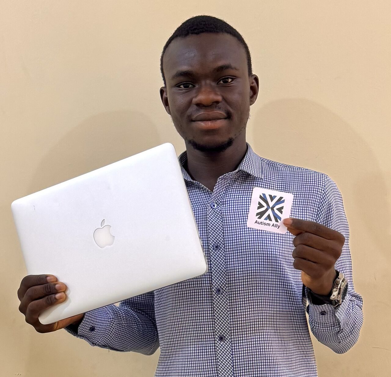 Abdulsalam, a medical student from Sokoto, holding a laptop and an Autism Ally sticker.